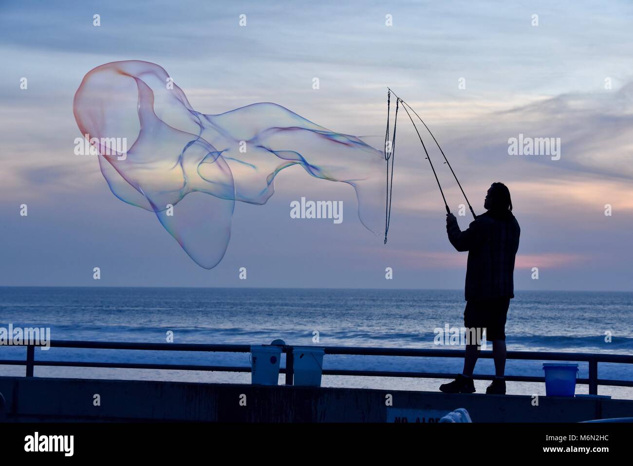 Interprète masculin de faire de gros, gros des bulles de savon au coucher du soleil avec vue sur l'océan Pacifique, Pacific Beach, San Diego, Californie, USA. Banque D'Images