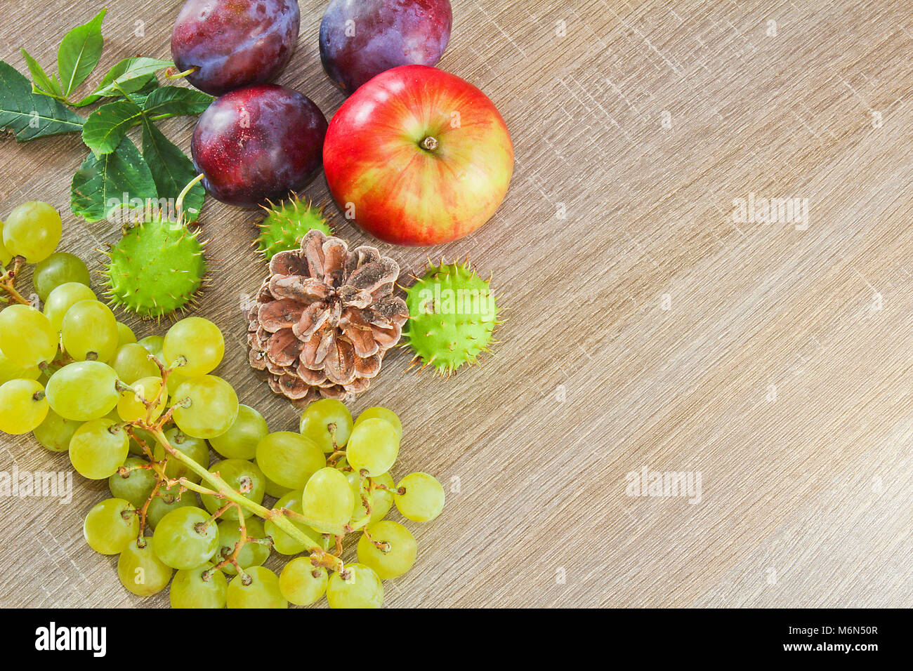 Fruits d'automne, cone, châtaignes, pommes, prunes et raisins sur fond en bois avec un espace réservé au texte Banque D'Images