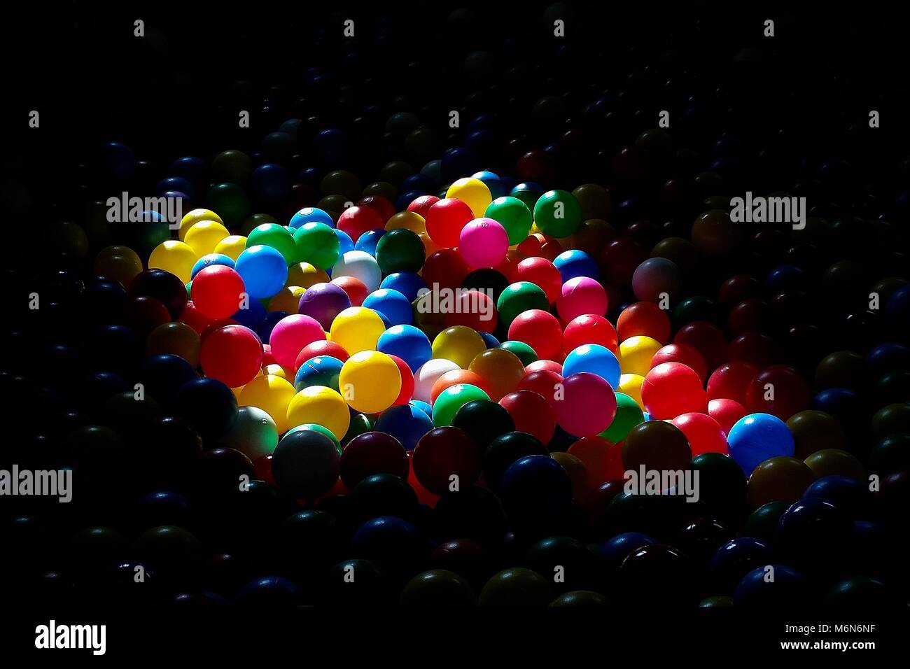 Billes en plastique coloré dans l'aire de jeux. Éclairé par le soleil, créant des gros contraste avec dark entourant. Banque D'Images