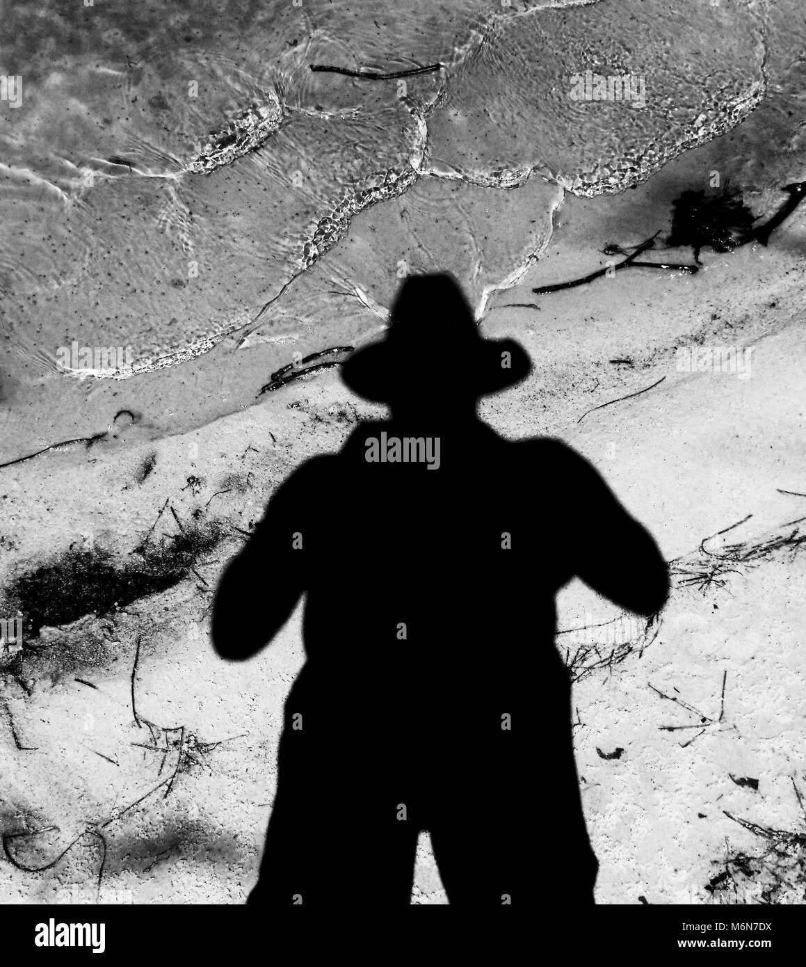 Photo en noir et blanc de silhouette d'un homme portant un chapeau à l'eau et le sable en arrière-plan Banque D'Images