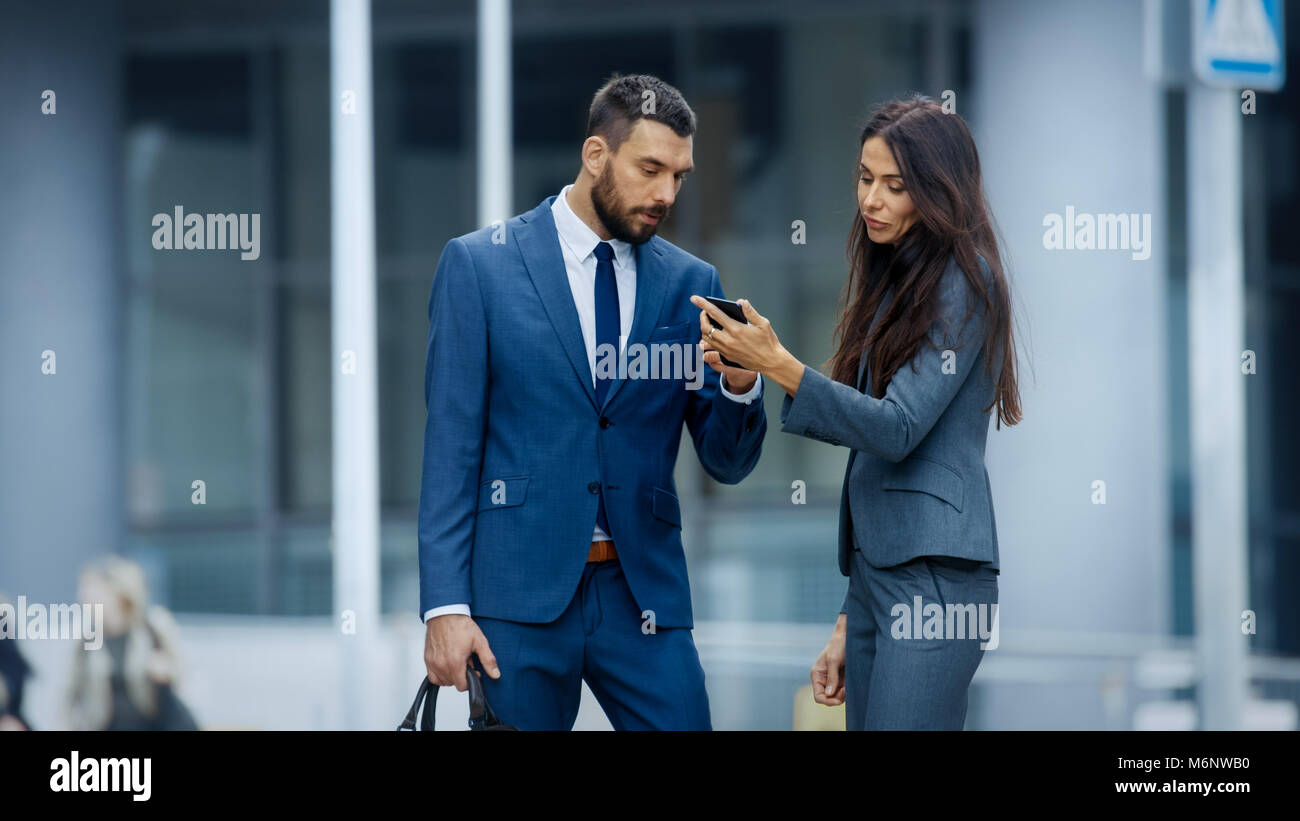 Femme d'affaires et homme d'affaires, utiliser Smartphone et parler sur l'animée rue grande ville. Look à la fois élégant, exquis. Banque D'Images