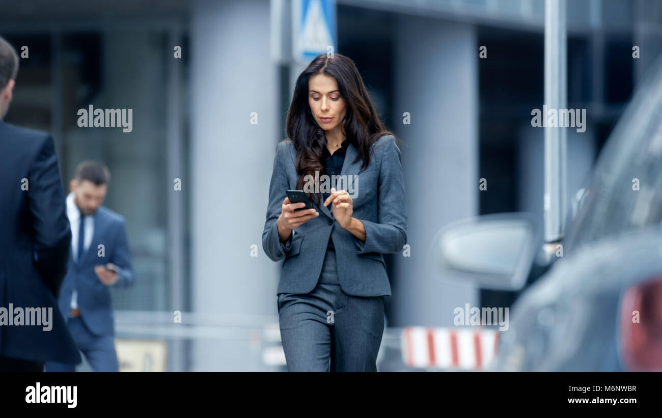 Femme d'affaires dans le costume sur mesure de marcher sur la grande ville animée Street dans le quartier des affaires, vérifie son Smartphone. Femme confiante sur rue. Banque D'Images