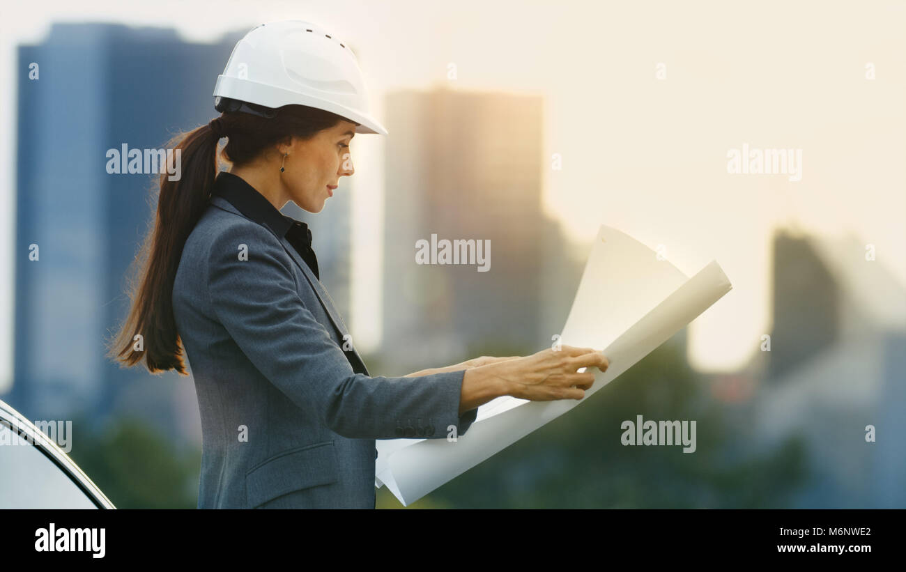 Femme Immobilier promoteur examine les ébauches de projet en étant debout. Grande ville avec des gratte-ciel en arrière-plan. Banque D'Images