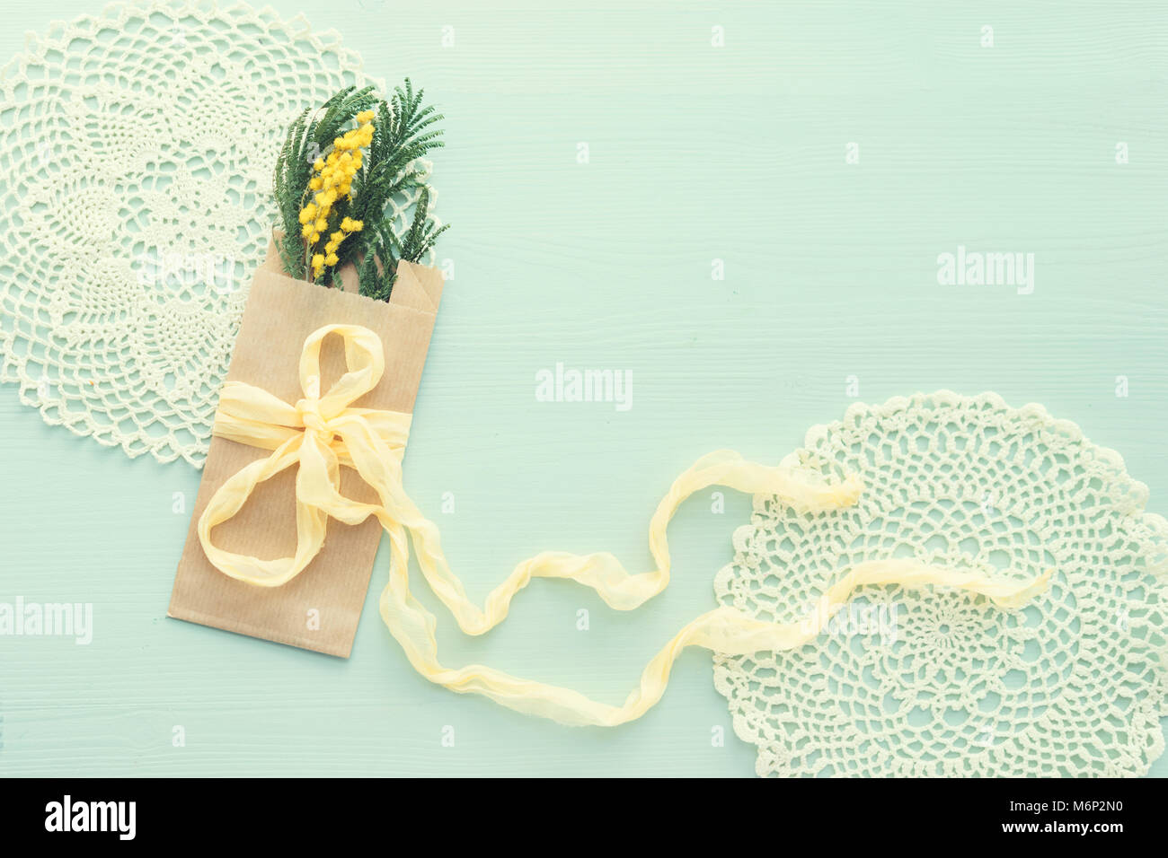 Le concept de la journée internationale de la femme mimosa brunch en enveloppe kraft sac sur fond bleu, soie jaune, bow place pour texte, napperon crochet tinte, Banque D'Images