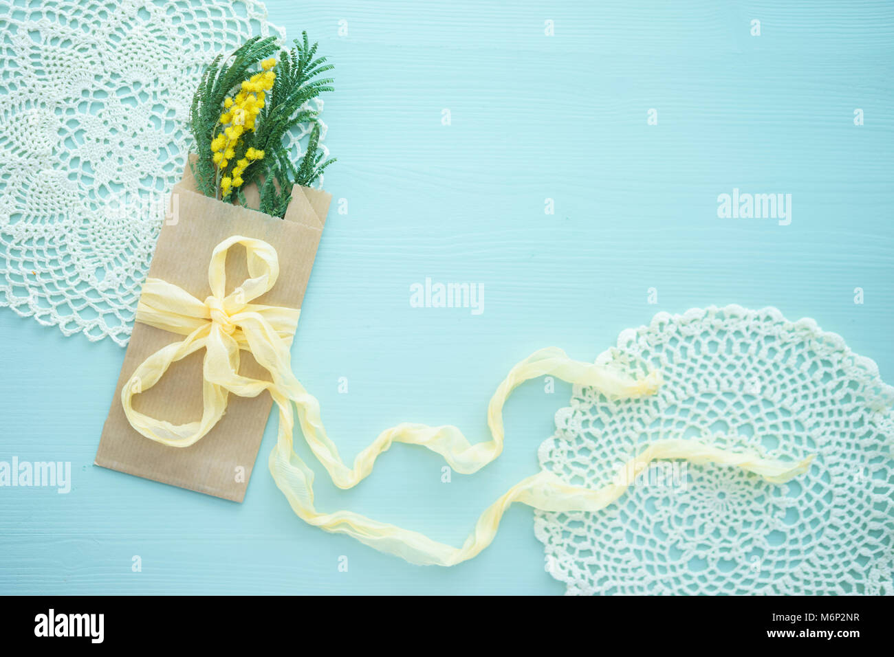Le concept de la journée internationale de la femme mimosa brunch en enveloppe kraft sac sur fond bleu, soie jaune, bow place pour texte, napperon au crochet Banque D'Images