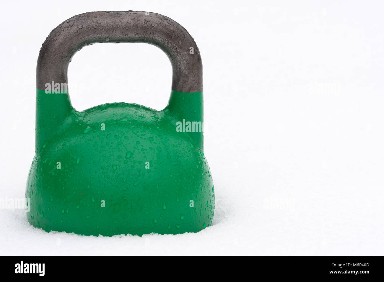 24kg kettlebell compétition verte couverte de gouttelettes d'eau à l'extérieur dans la neige. Copie potentiel espace à droite de kettlebell. Banque D'Images