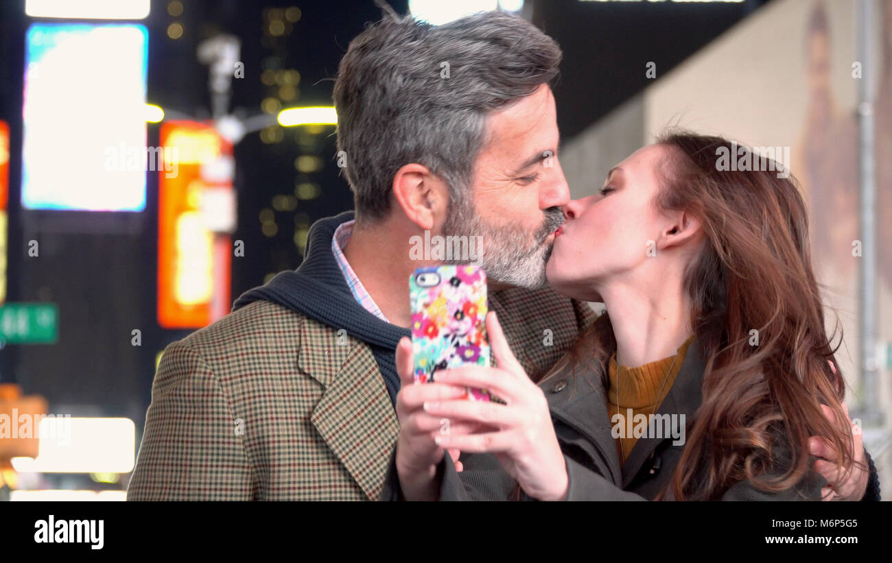 Un couple romantique en prenant une photo avec selfies smart téléphone cellulaire en plein milieu de Times Square, New York Le New Years Eve célébration à minuit. Jour Nuit Banque D'Images