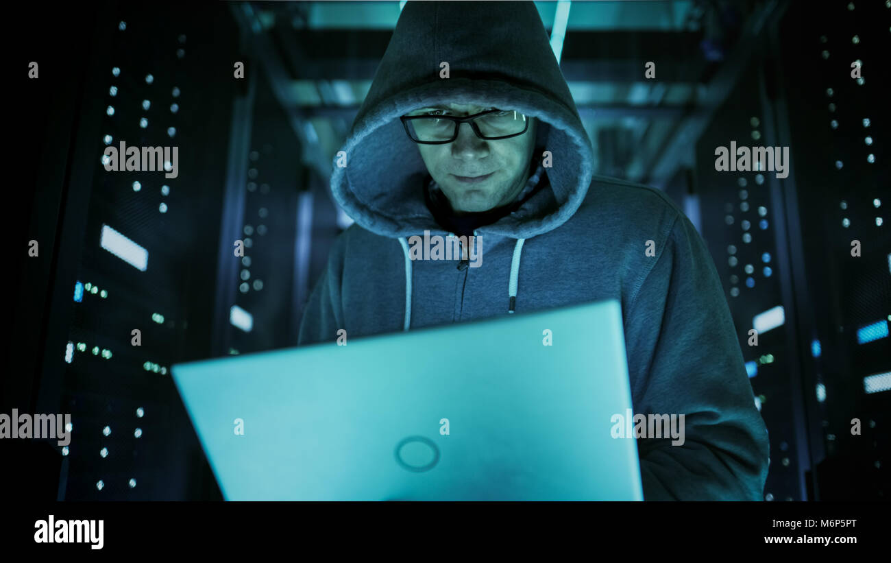 Close Close-up shot of computer hacker in Hoodie, Holding Laptop. Il anneaux brisés dans un centre de données de l'entreprise. Banque D'Images
