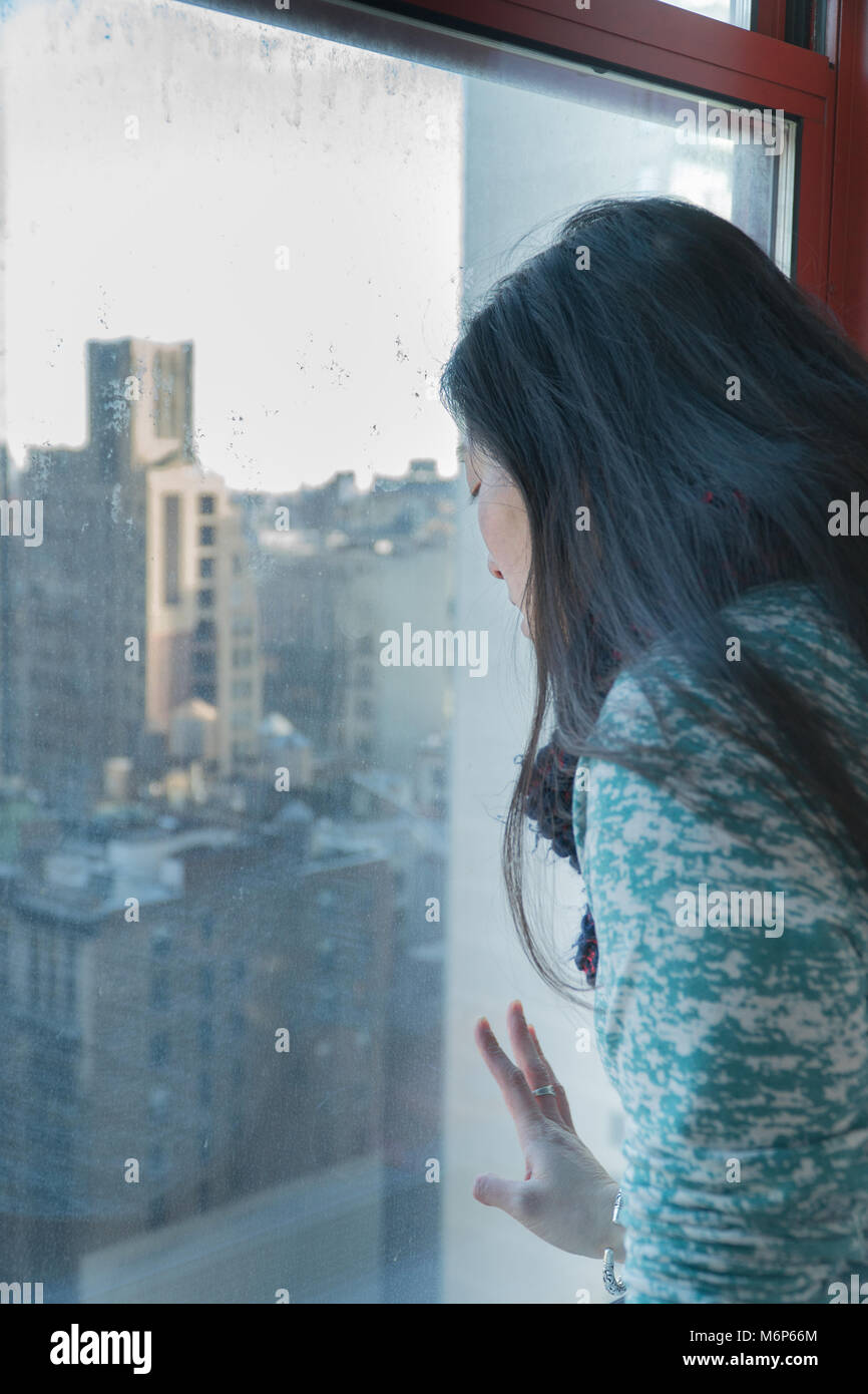 Young Asian woman staring à travers une fenêtre vue donnant sur les toits de la ville de New York sur une journée ensoleillée. Voyages touristiques attractions - voir Ve Banque D'Images