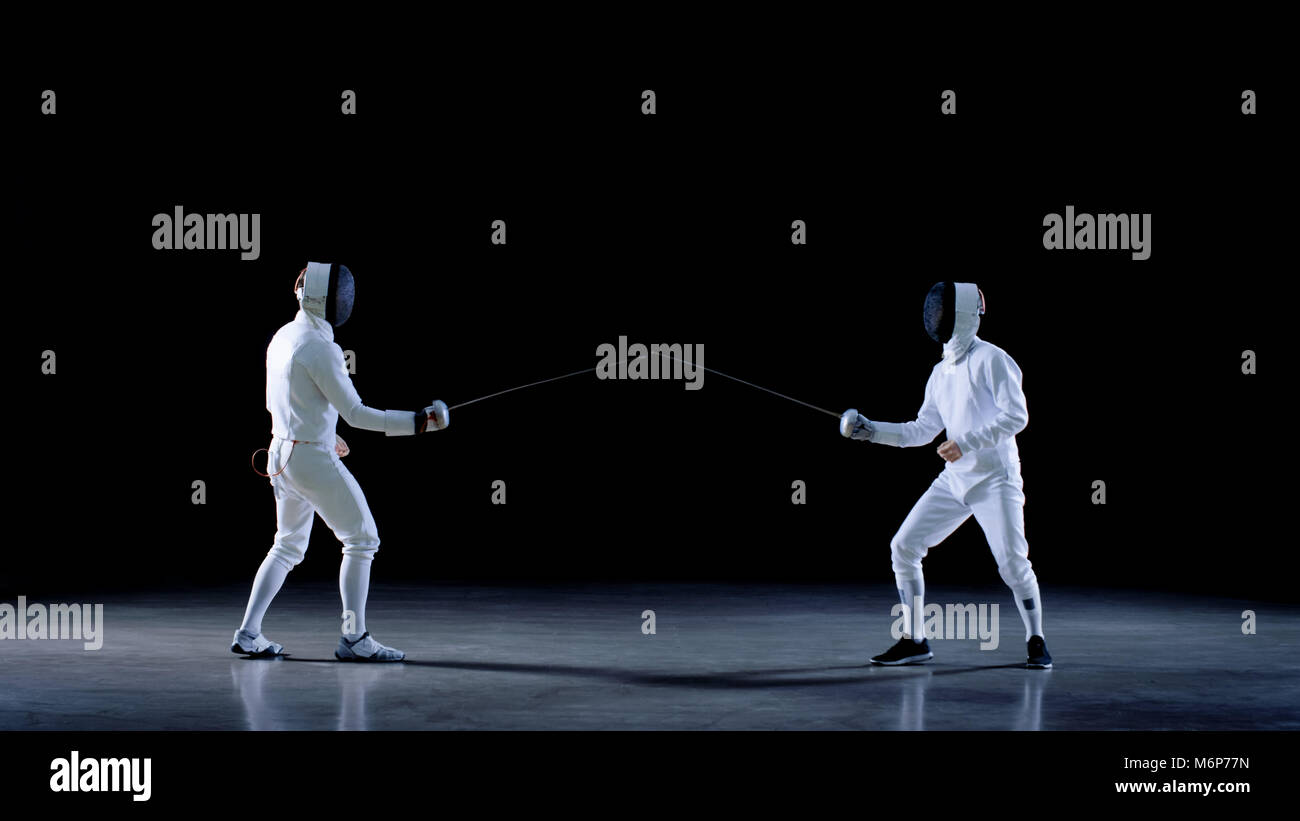 Deux jeunes tireurs professionnels public salue, mis sur les masques et commencer les combats à l'Épée Match. Shot isolé sur fond noir . Banque D'Images