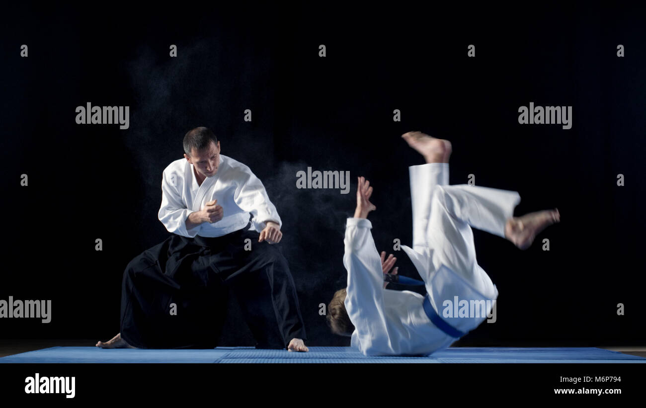 Maître d'Arts Martiaux portant des Hakamas enseigne aux jeunes élèves la technique d'Aikido de jeter sur l'Épaule Shot isolé sur fond noir. Banque D'Images