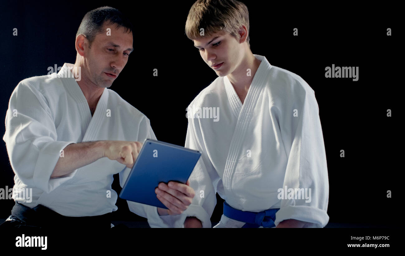 Maître d'Arts Martiaux portant des Hakamas enseigne aux jeunes élèves Aikido technique avec l'aide de l'ordinateur tablette. Shot isolé sur fond noir. Banque D'Images