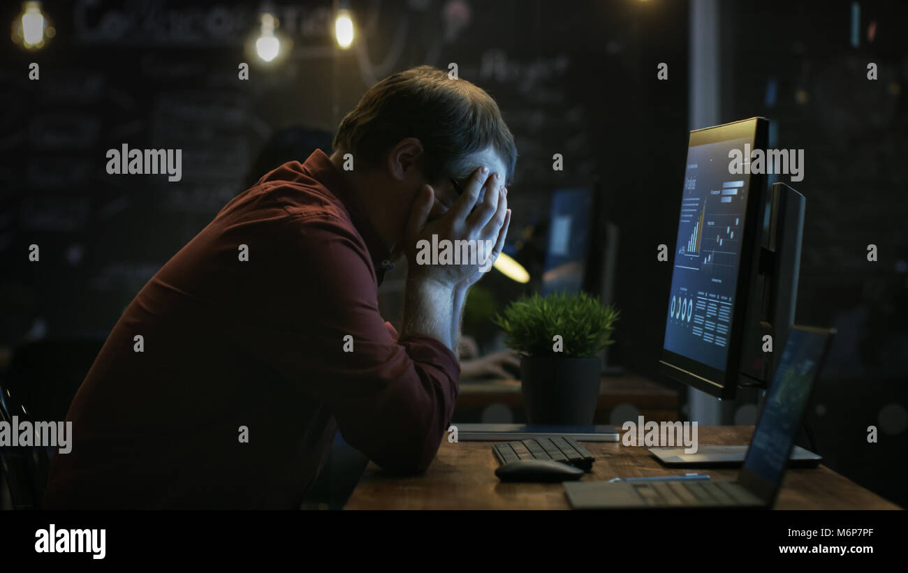 Le financier a souligné la table Hits avec son poing dans la frustration et couvre son visage dans les mains. Il travaille sur un ordinateur personnel avec Statistique Banque D'Images