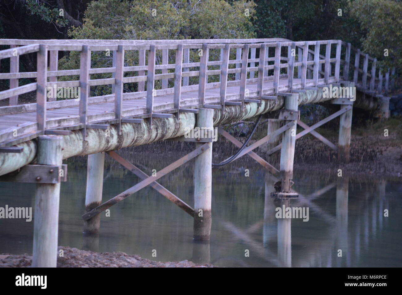 Scène pastel, image au crépuscule d'une passerelle en bois décolorée sur des poteaux en bois ronds se reflétant dans creek à Moonee Beach, Nouvelle-Galles du Sud, Australie Banque D'Images