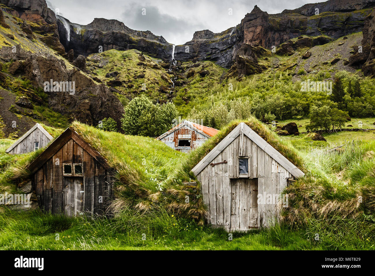 Maisons et gazon islandais canyon rocheux avec une cascade dans le fond près de Kalfafell vilage, Sud de l'Islande Banque D'Images