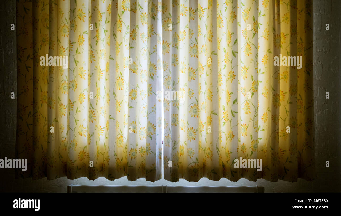 Tôt le matin, le soleil qui rayonne à travers une fissure dans une paire de double rideaux panneau fermé. Banque D'Images