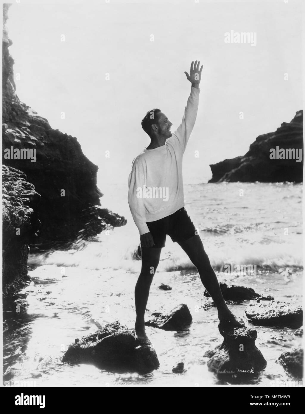 L'acteur Fredric March debout avec bras soulevé on Rocky Beach, Californie, USA, début des années 40 Banque D'Images