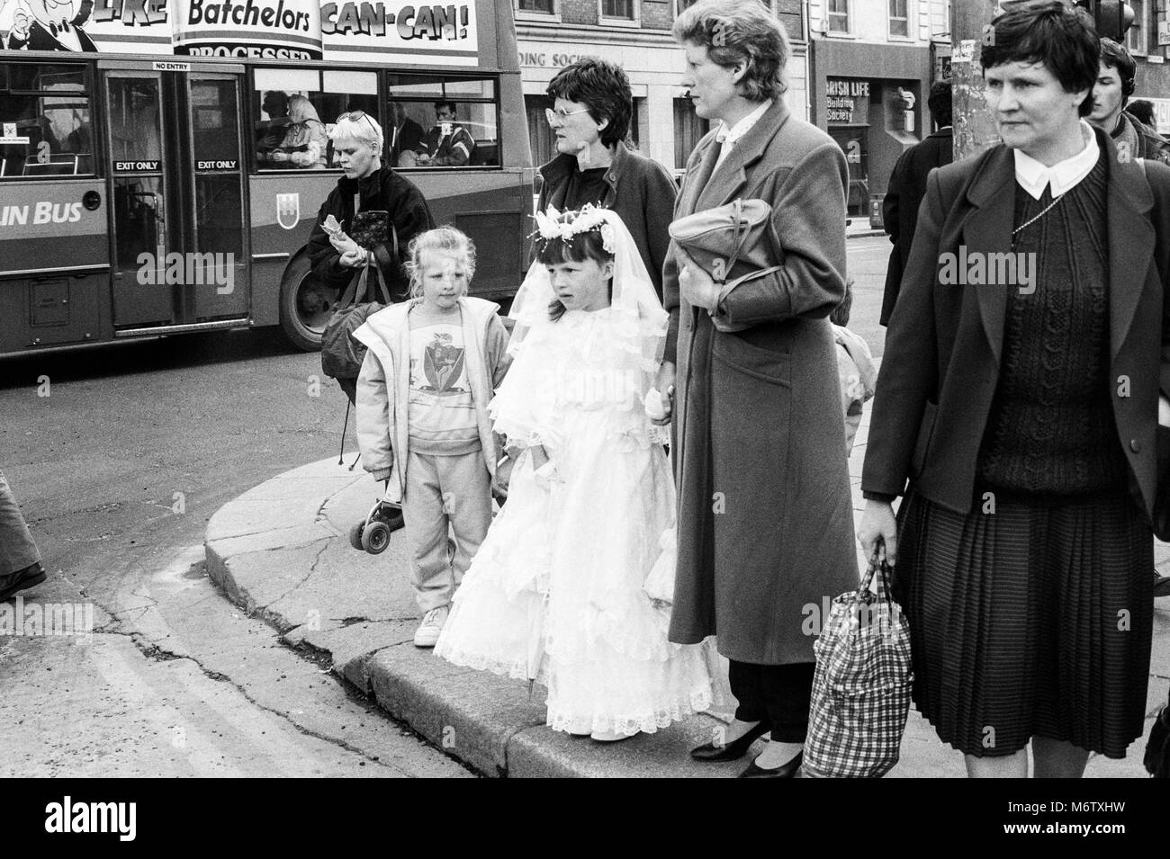 Jeune fille en robe de première communion sur coin de rue en attendant de traverser la route, Westmoreland Street, Dublin, Irlande, photographie d'archives de Avril 1988 Banque D'Images