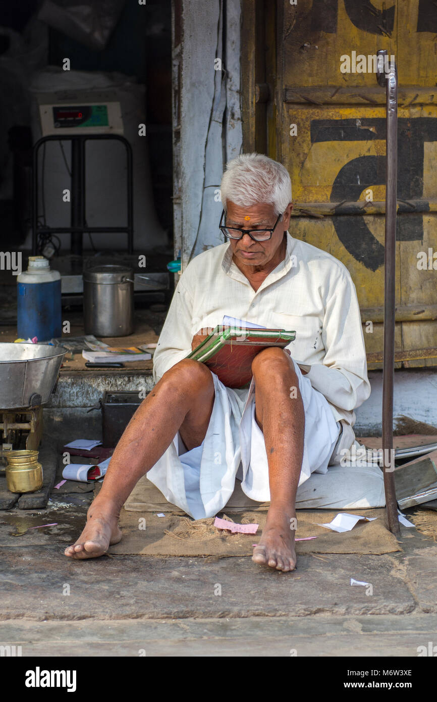 Homme indien aux cheveux blancs portant un dhoti blanc et une chemise, assis dans la rue écrivant dans un journal ou un livre à Samode, Rajasthan, Inde Banque D'Images
