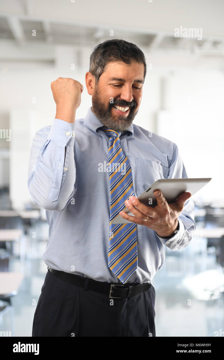 Hispanic businessman celebrating tandis qu'à la tablette électronique à l'intérieur d'immeuble de bureaux Banque D'Images