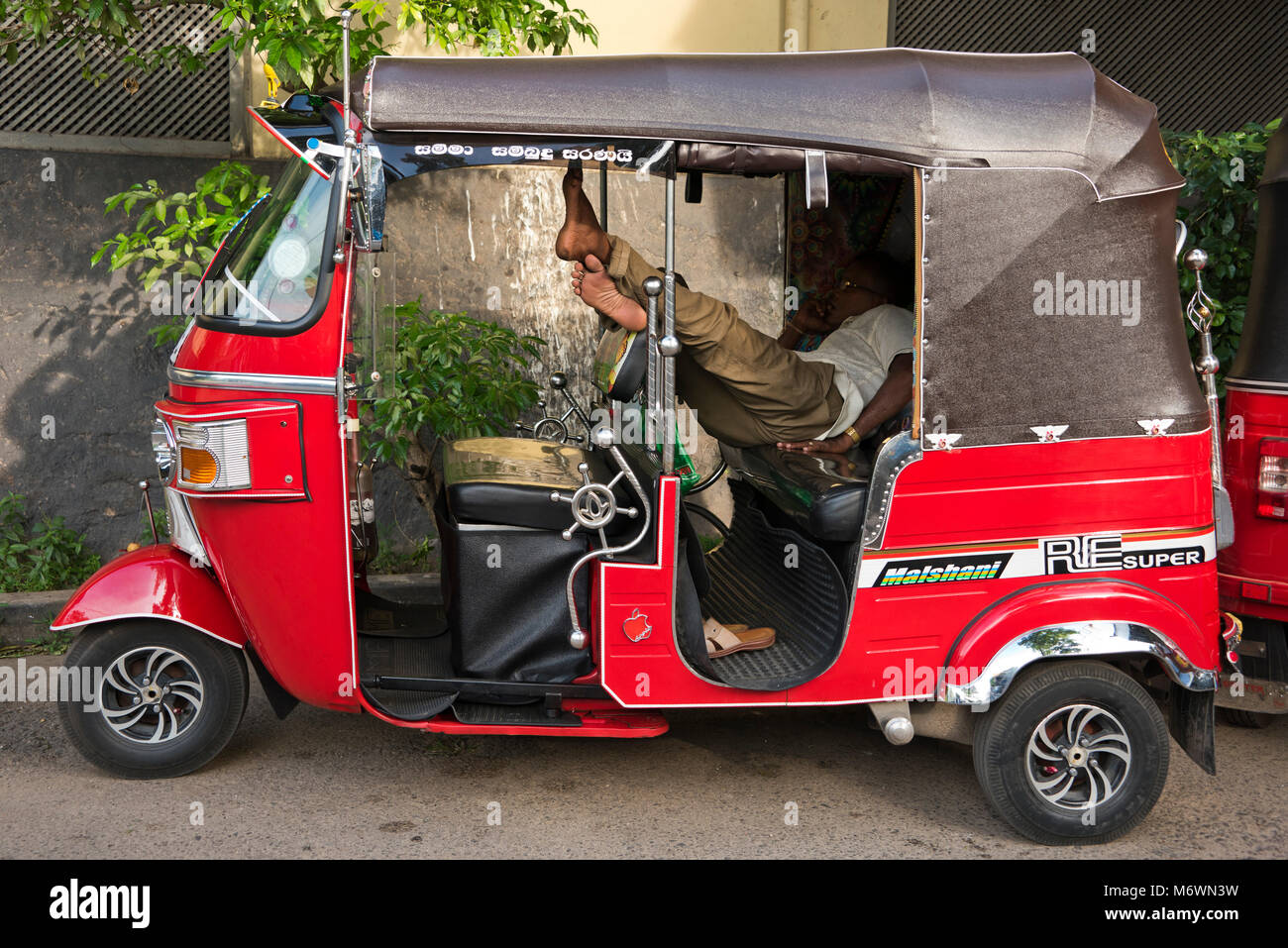 Vue horizontale d'un conducteur de pousse-pousse endormi à l'arrière de son véhicule à Colombo, Sri Lanka. Banque D'Images