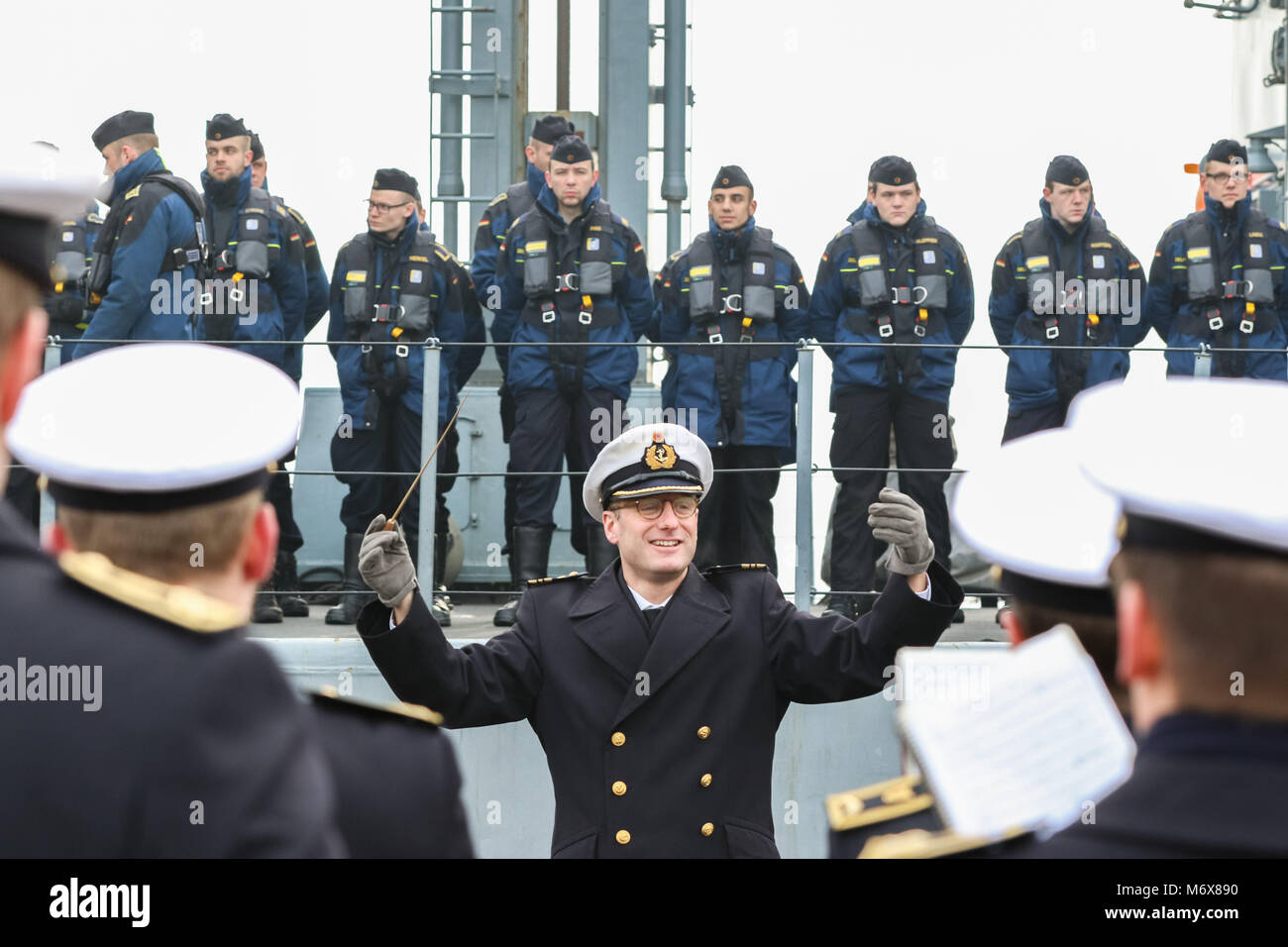 Wilhelmshaven, Allemagne. 07 mars 2018, les troupes de marine à bord de l'attention la frégate de la marine allemande 'Bayern' comme un orchestre de cuivres de la marine (avant) joue une sérénade au départ du navire à partir de la base navale. Le "Bayern" est de mettre les voiles pour une période de six mois de déploiement de l'OTAN dans la mer Egée. Photo : afp/Assanimoghaddam Mohssen Banque D'Images