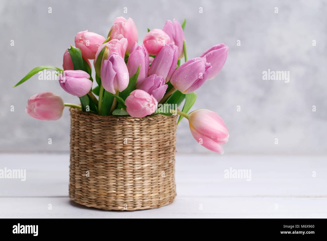Bouquet de tulipes roses dans un panier en osier sur fond gris clair Banque D'Images