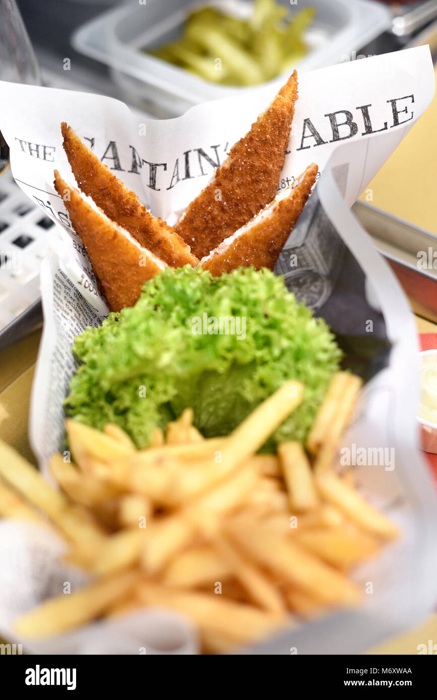 Crumbed des portions de poisson frit servi avec frites et salade verte à froufrous frais sur journal dans un restaurant ou des pêches Banque D'Images