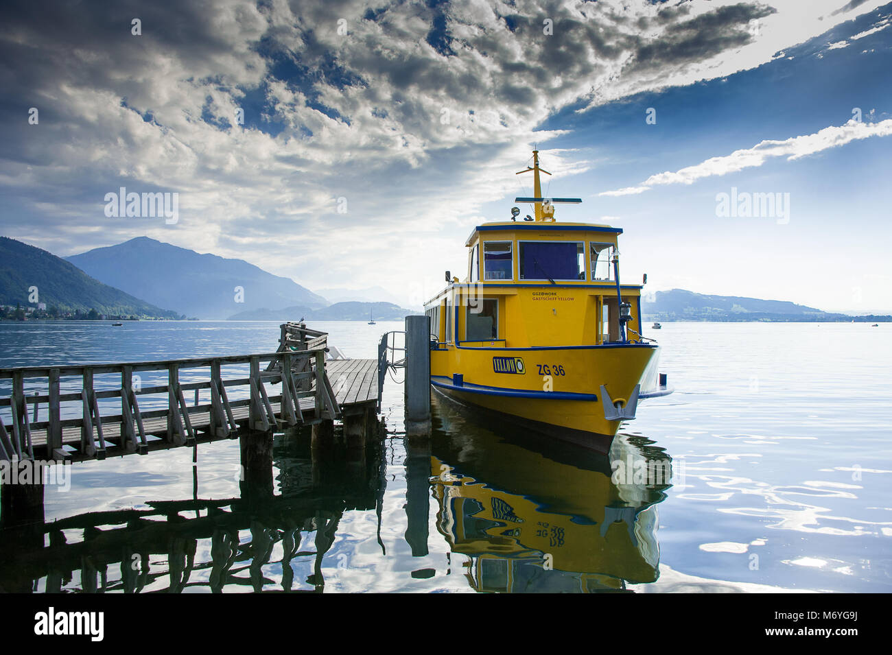 Zug, Suisse. Ciel bleu, nuages et réflexions. Barge jaune ancrée à la jetée sur le lac de Zoug. Banque D'Images