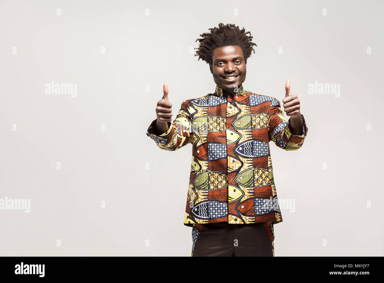 Homme africain en vêtements traditionnels dents sourire, showing Thumbs up, loke signe. Piscine, isolé sur fond gris Banque D'Images
