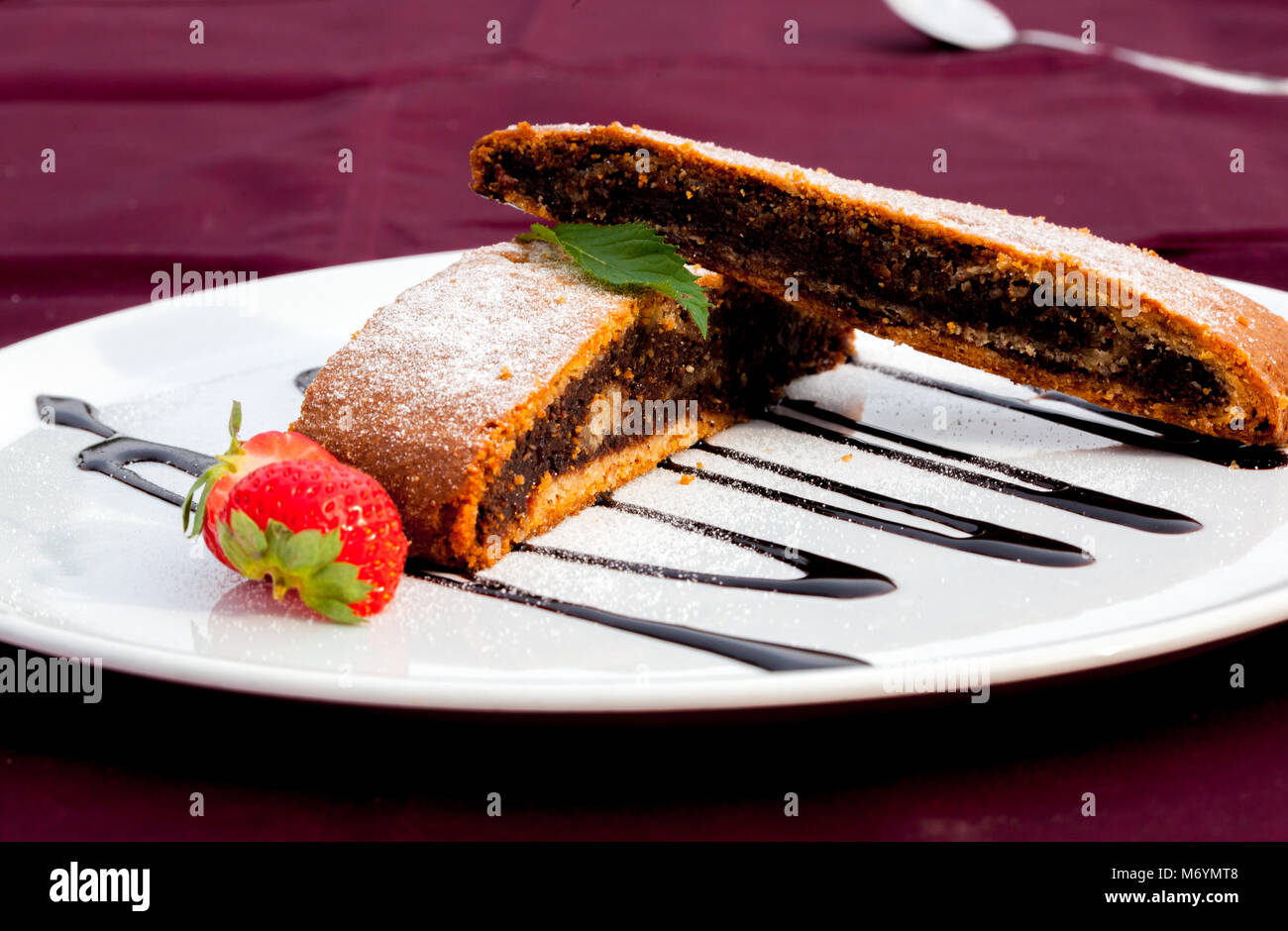 Une tranche de graines de pavot gâteau sur une assiette blanche décorée de laisser la menthe, chocolatte et fraise. Banque D'Images
