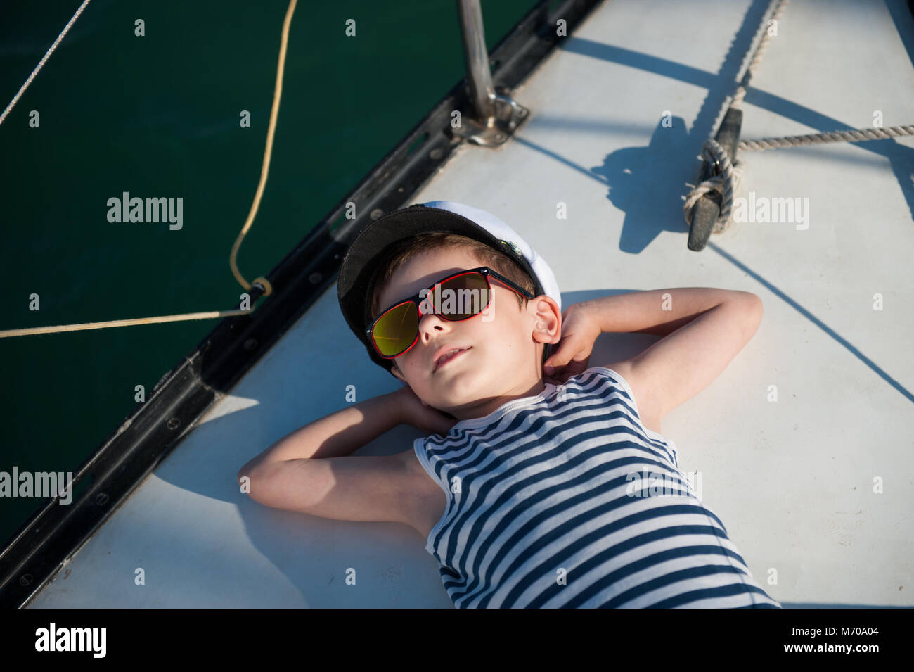 Beau petit enfant à lunettes couché sur conseil d'yacht blanc bénéficiant Banque D'Images