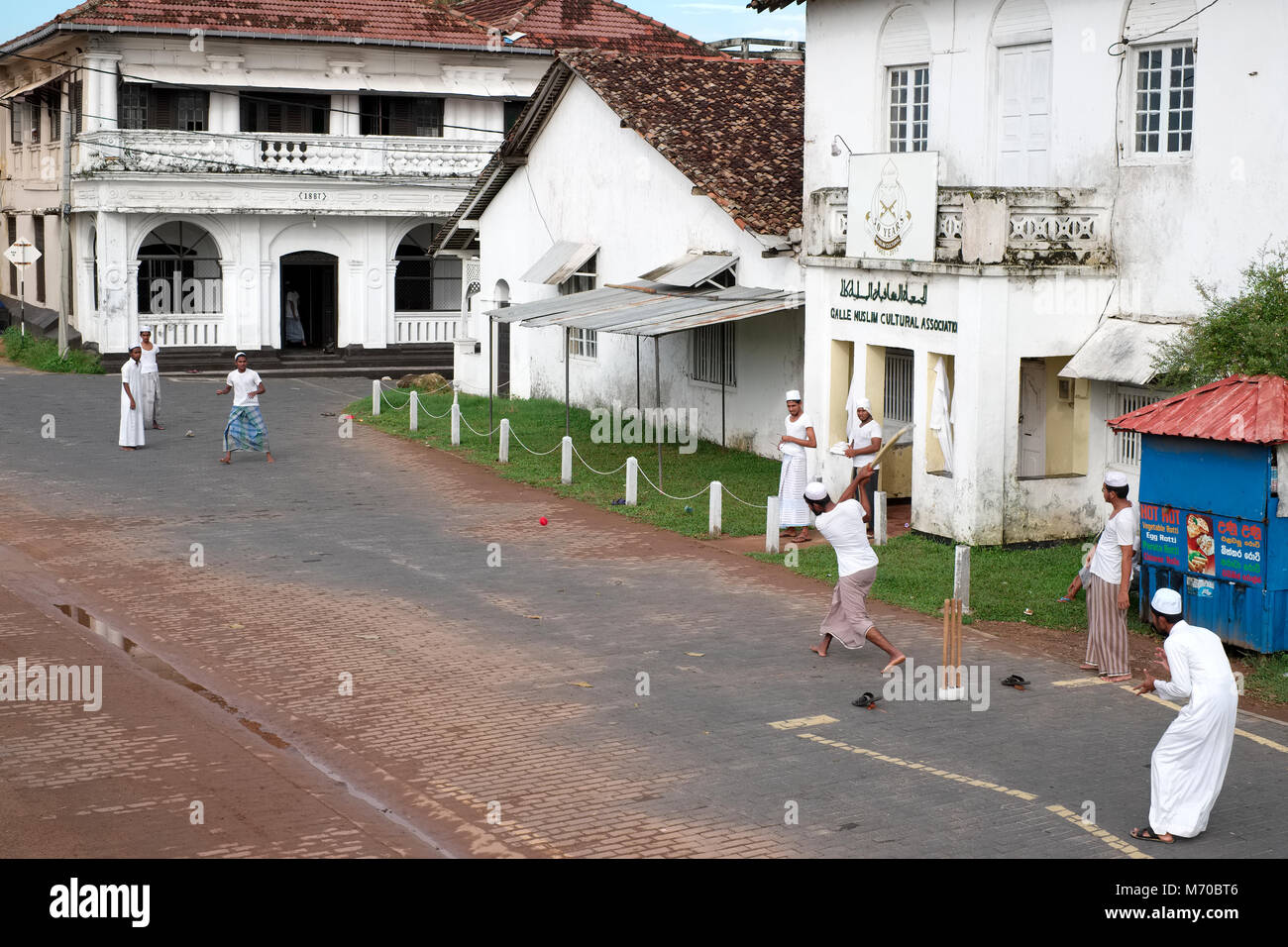 Les jeunes hommes jouer au cricket dans la rue devant l'Association culturelle musulmane Galle Galle Fort en construction au Sri Lanka Banque D'Images