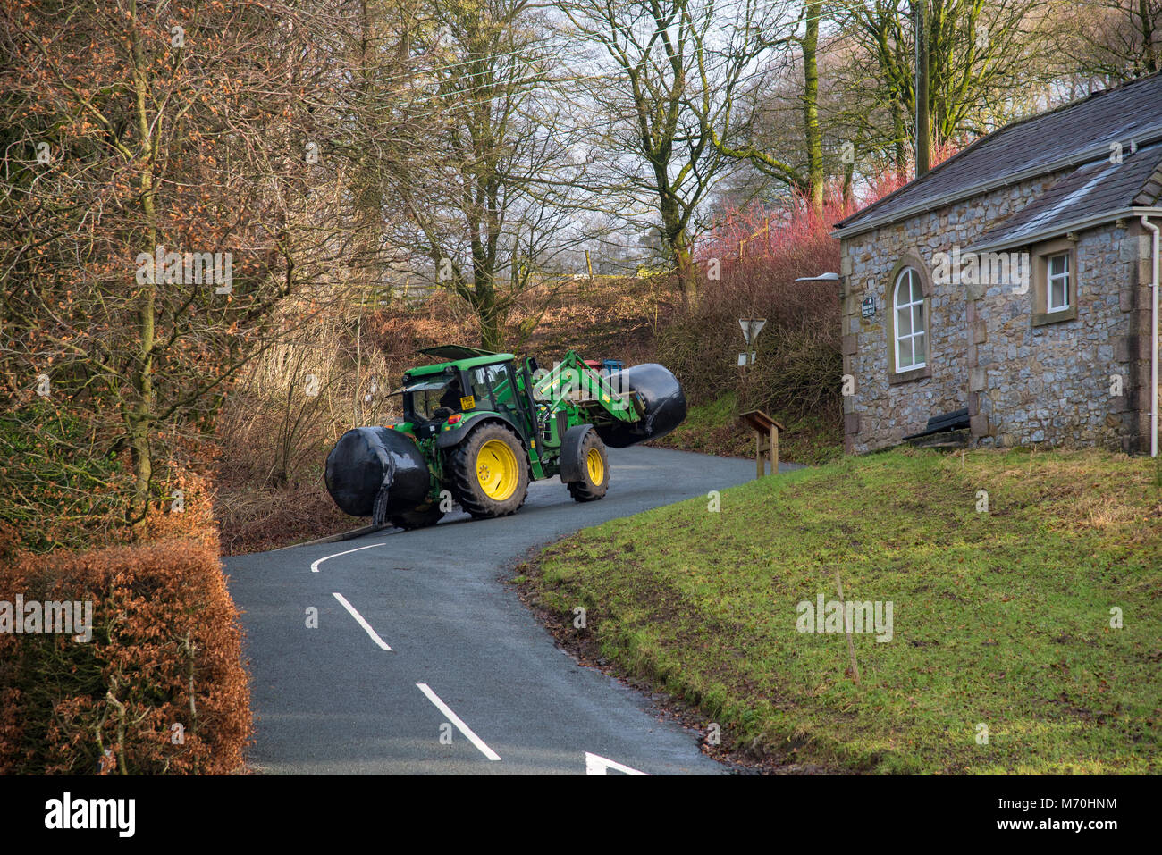 Un tracteur John Deere avec deux balles de fourrage ensilé remontant d'une route de campagne, Whitewell, Clitheroe, Lancashire. Banque D'Images