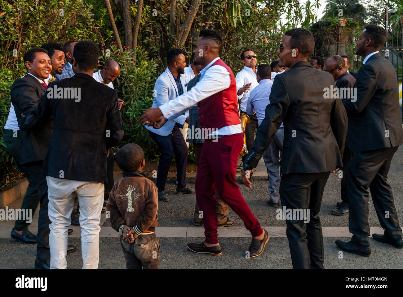 Les membres masculins d'un Cortège de danser dans la rue vu par un garçon de la rue embroussaillé, Addis-Abeba, Ethiopie Banque D'Images