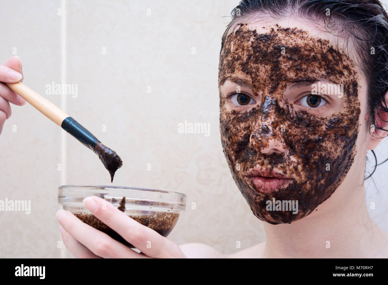 Modèle de race blanche entre l'âge de 20 à 29 ans à l'aide d'un exfoliant visage café pour son visage et sacs d'oeil. Banque D'Images