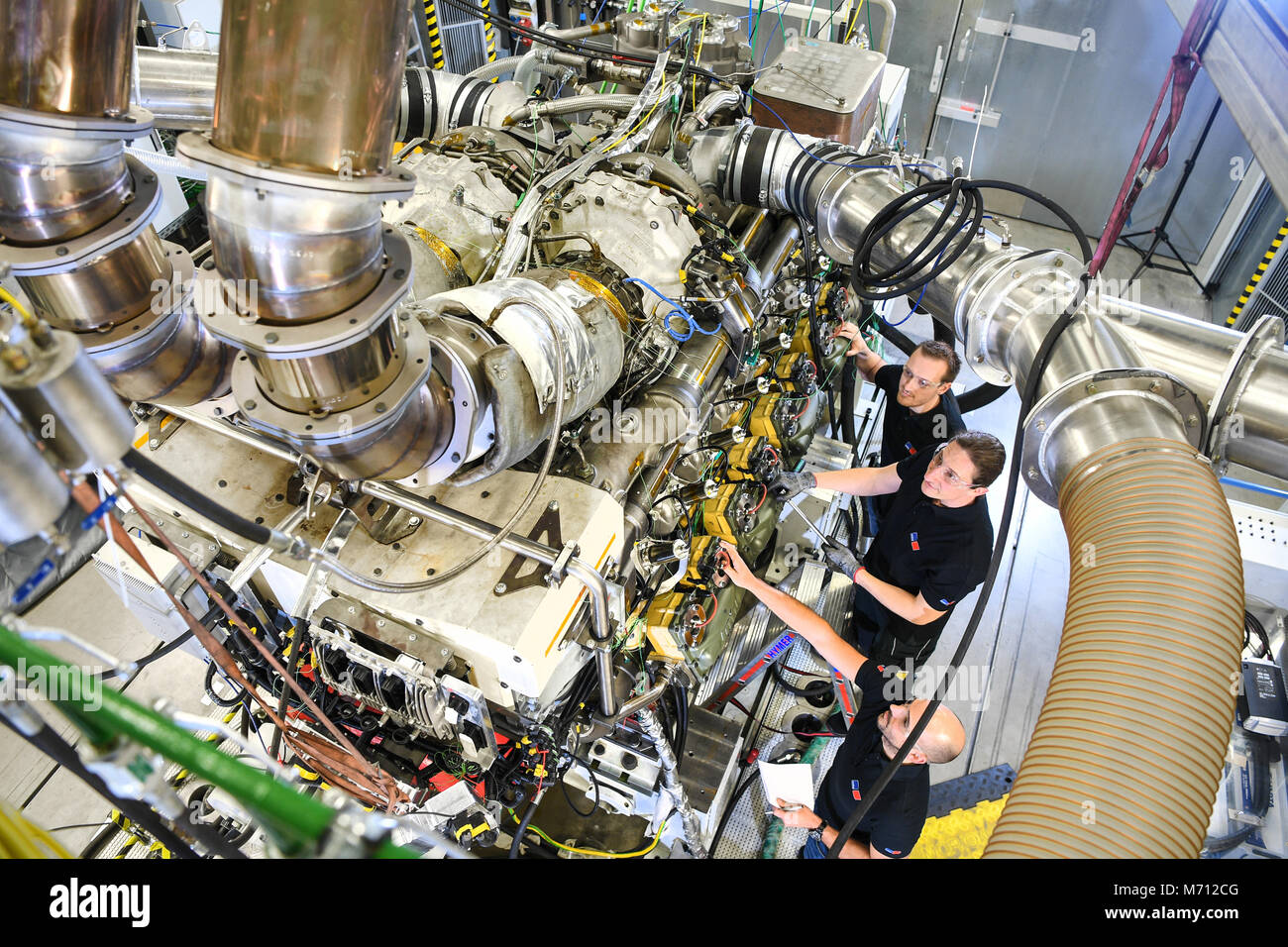 07 mars 2018, l'Allemagne, Friedrichshafen : Un technicien et deux  ingénieurs travaillent sur un moteur à gaz de MTU à Rolls-Royce un MTU banc  d'essai. Le moteur à gaz 16 cylindres de