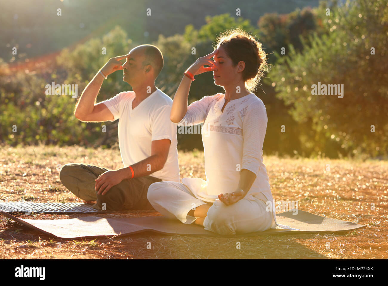 Jeune couple pratiquant la respiration yogique technique appelée Pranayama. Ils sont assis sur leurs tapis de yoga à l'extérieur pendant le coucher du soleil. Banque D'Images