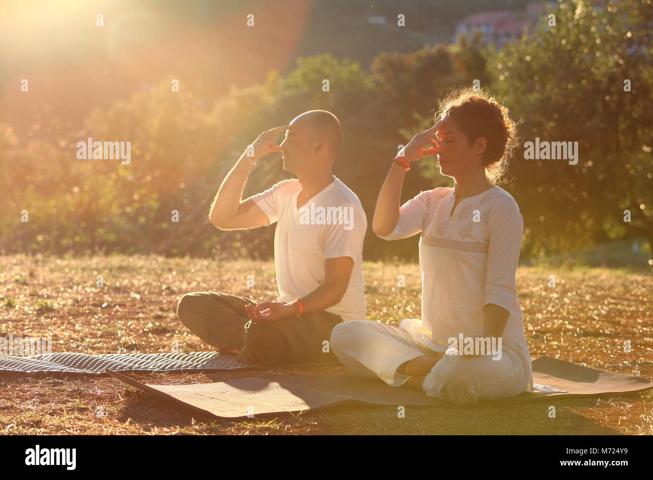 Jeune couple pratiquant la respiration yogique technique appelée Pranayama. Ils sont assis sur leurs tapis de yoga à l'extérieur pendant le coucher du soleil. Banque D'Images