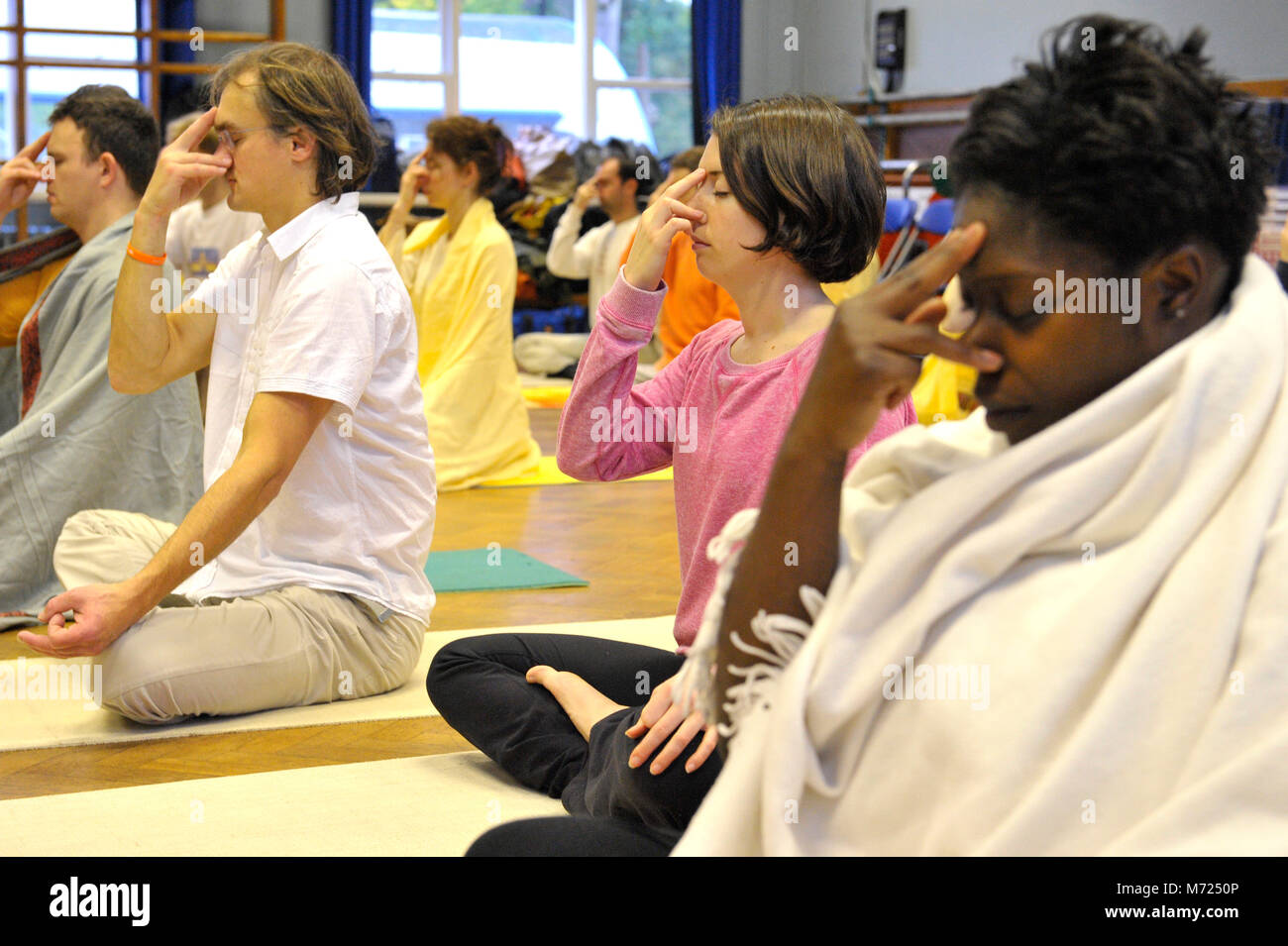 Groupe de jeunes gens pratiquant la respiration yogique mixte technique appelée pranayama dans une salle. Assis sur leurs tapis de yoga sur le parquet. Banque D'Images