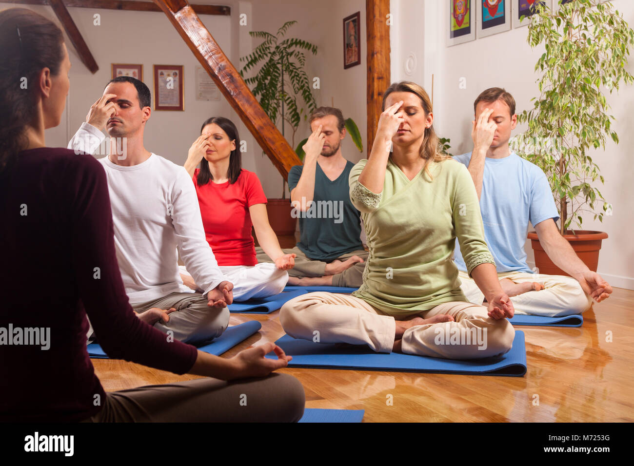 Les jeunes gens pratiquant la respiration yogique technique appelée Pranayama. Guidé par un instructeur assis sur bleu tapis de yoga sur le parquet à l'intérieur. Banque D'Images
