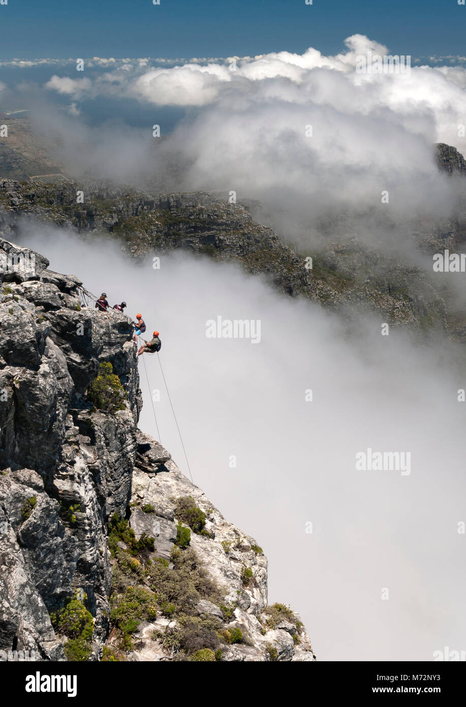 Abseilers la descente en rappel sur le sommet de la Table Mountain à Cape Town avec le nuage-enveloppé Douze Apôtres montagnes en arrière-plan. Banque D'Images