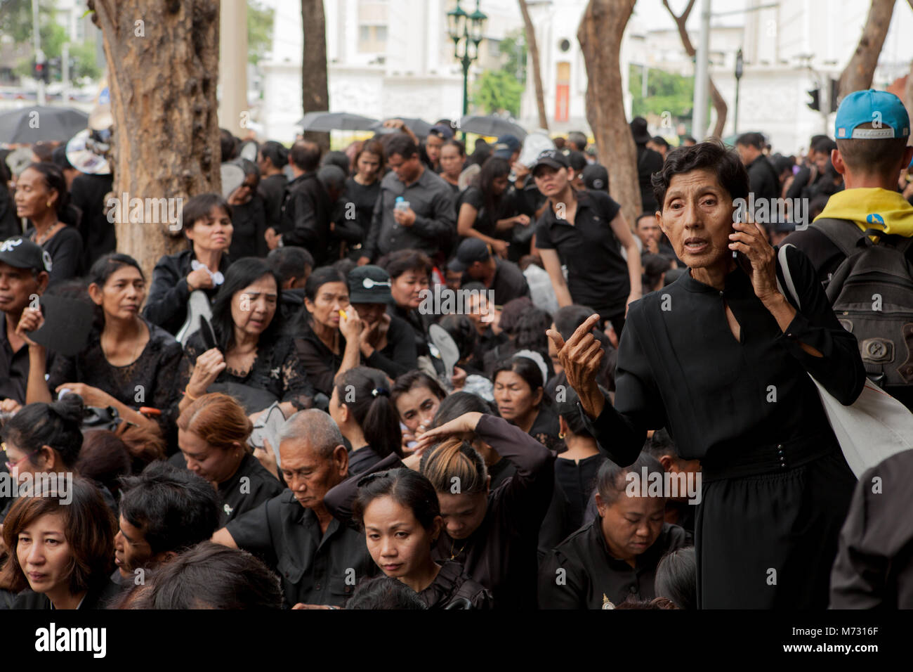 Foule de gens sur le trottoir en Ratchadamnoen Road à Bangkok le jour de la Crémation Royale, assis en attente dans leurs vêtements noirs Banque D'Images