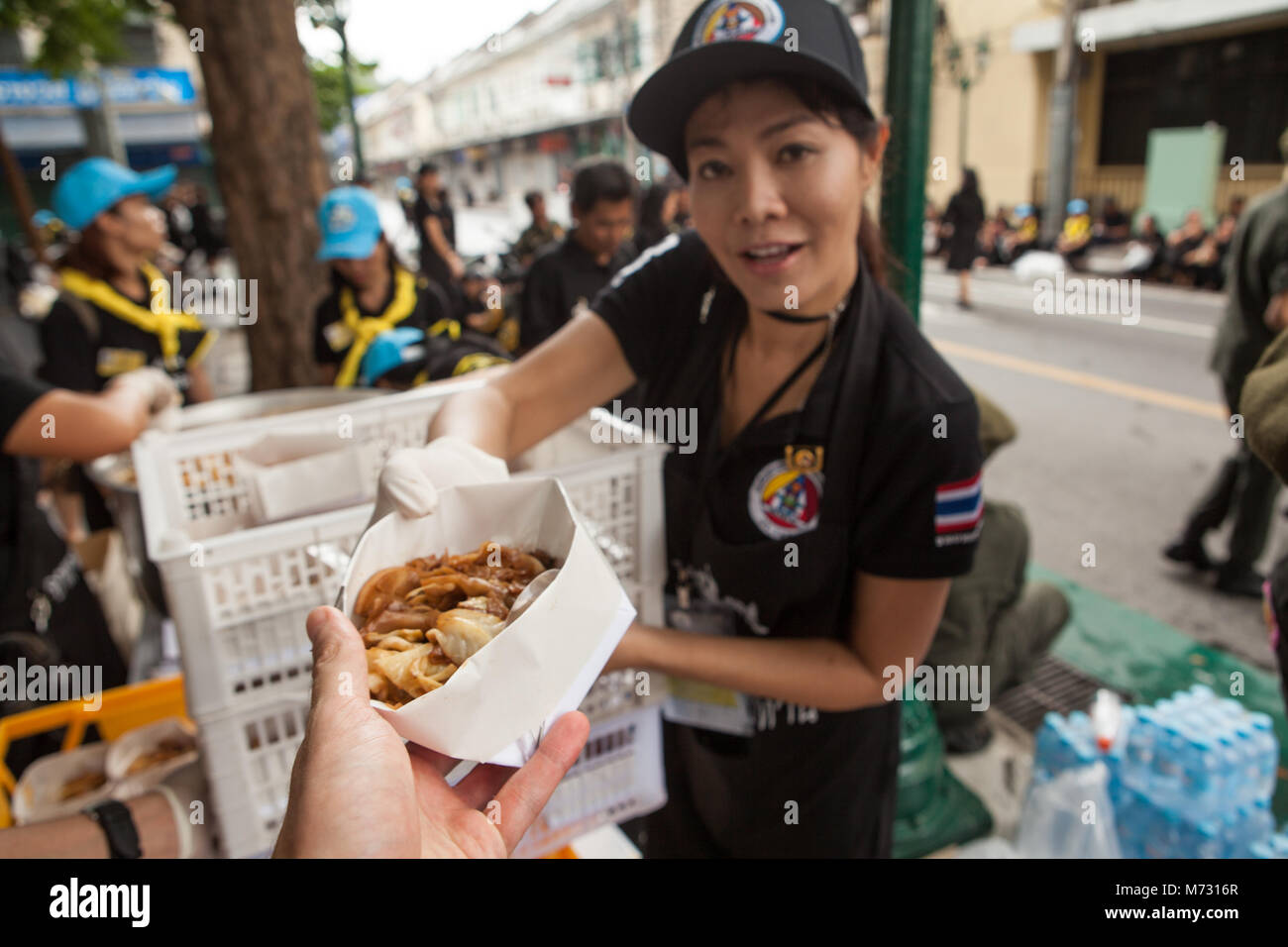 Une jeune fille bénévole offrant gratuitement de la nourriture à un participant à la crémation royale du roi thaïlandais à Bangkok Banque D'Images