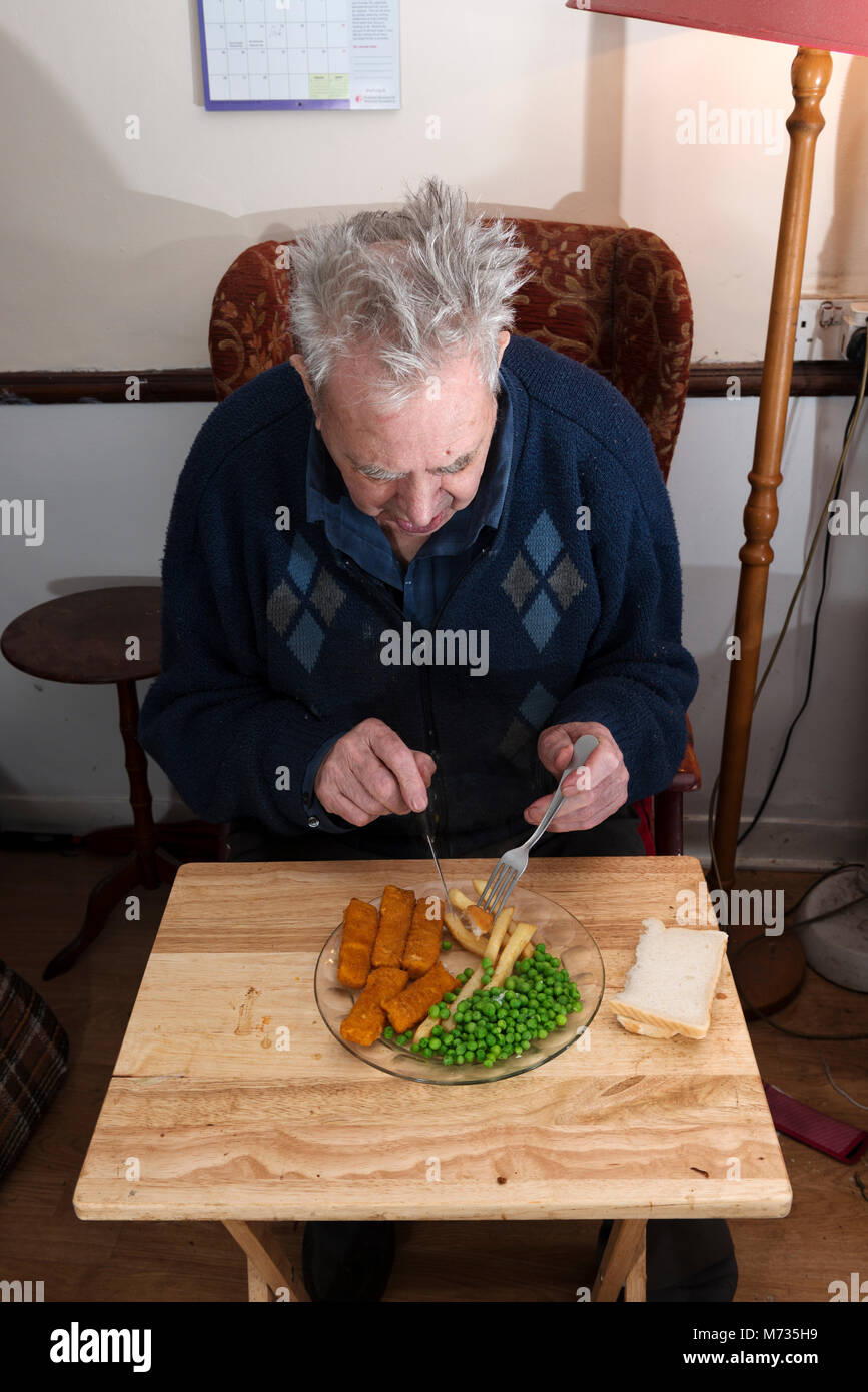 Un homme âgé vivant seul manger des bâtonnets de poisson, les croustilles et les pois pour le déjeuner Banque D'Images