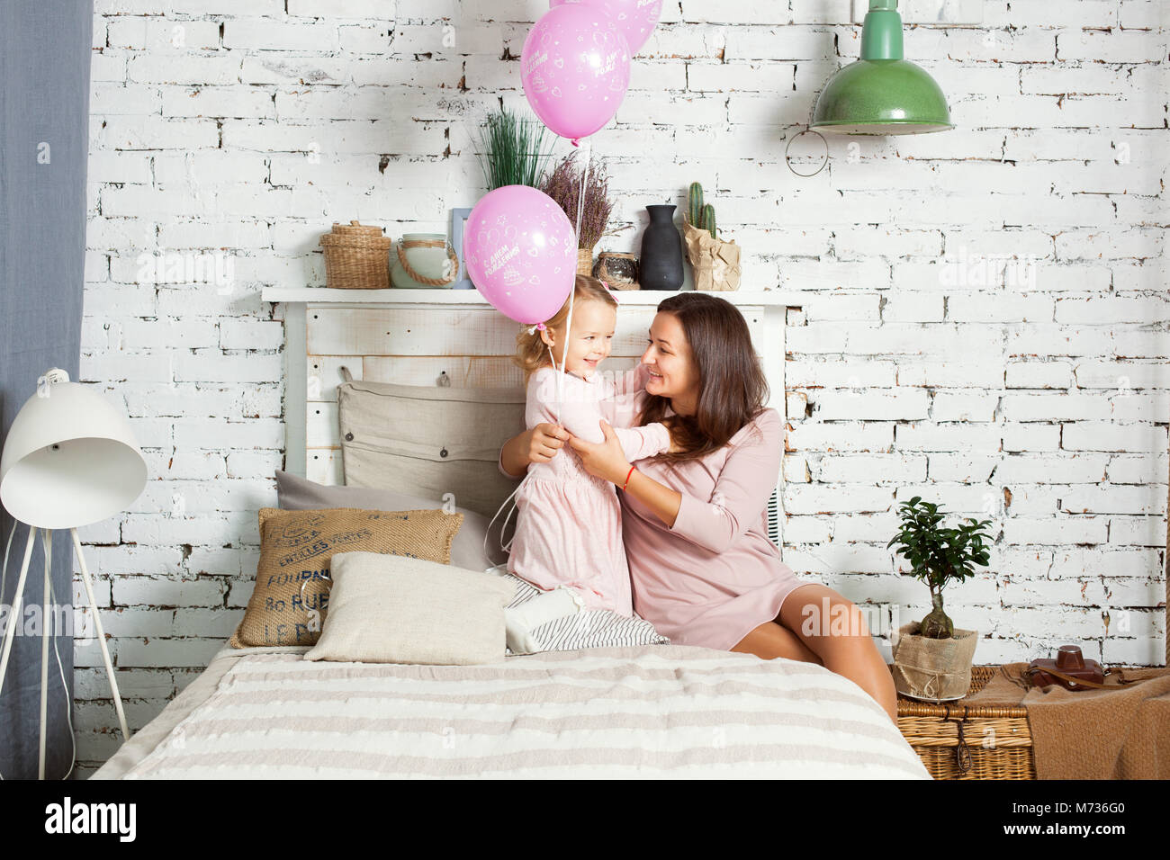 Mère et fille sont assis sur le lit. Little girl holding balloons in hands Banque D'Images