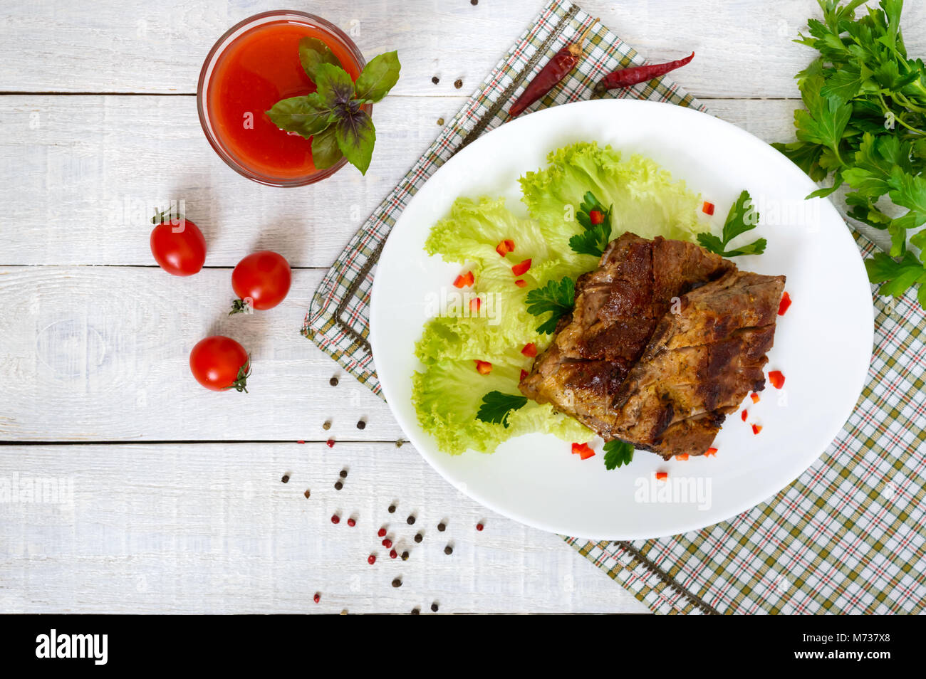 Côtes de porc frits sur une plaque avec les verts et le jus de tomate sur un fond de bois blanc. Banque D'Images