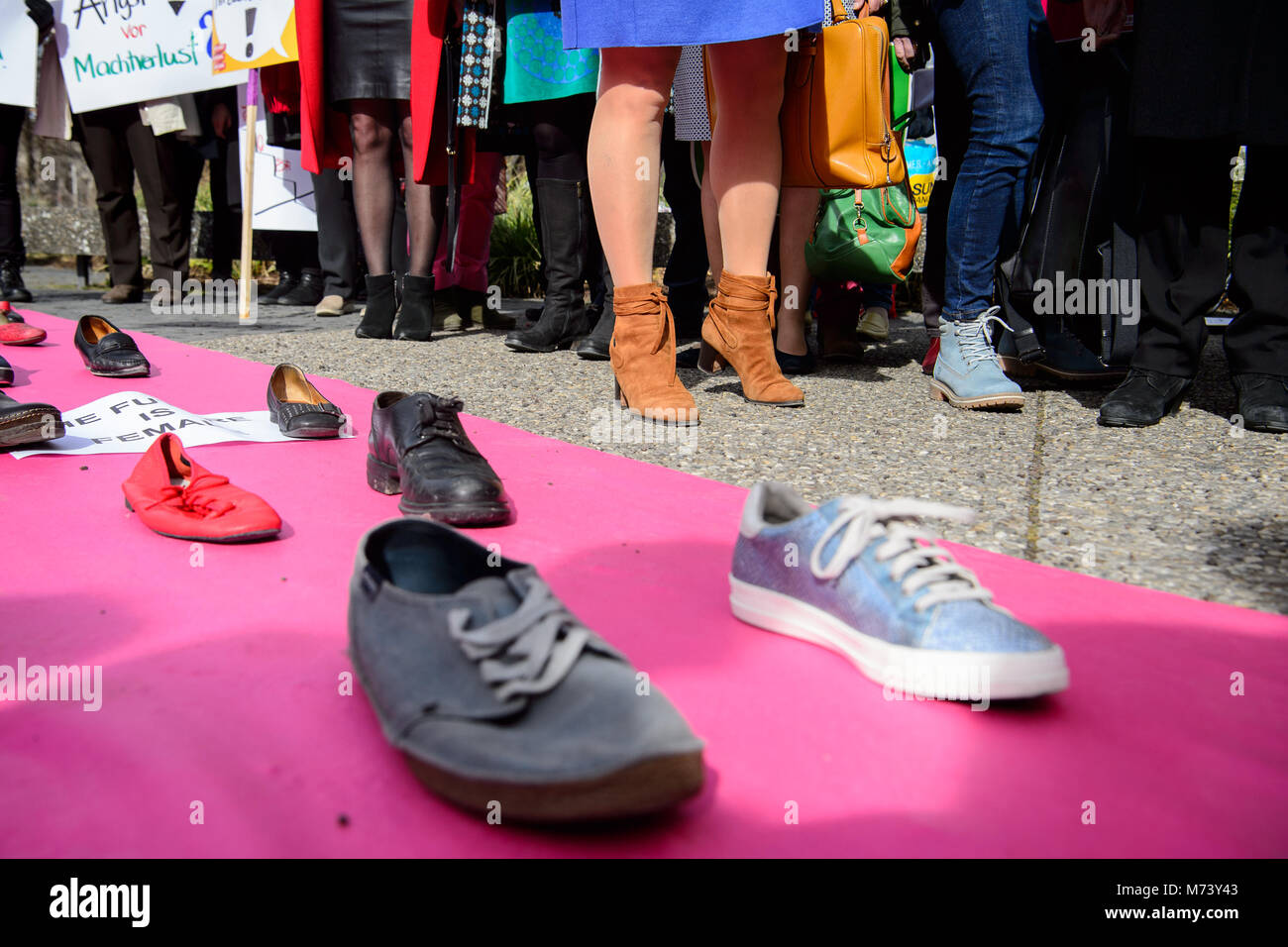 08 mars 2018, l'Allemagne, Stuttgart : Les femmes debout par un tapis, qui est couverte d'affiches. Le Conseil d'État sont des femmes à l'aide de cette campagne de lutte pour l'égalité entre les hommes et les femmes : Un tapis rose avec une rangée de paires de chaussures chaussures unique composé de des hommes et des femmes. Photo : Sina Schuldt/dpa Banque D'Images