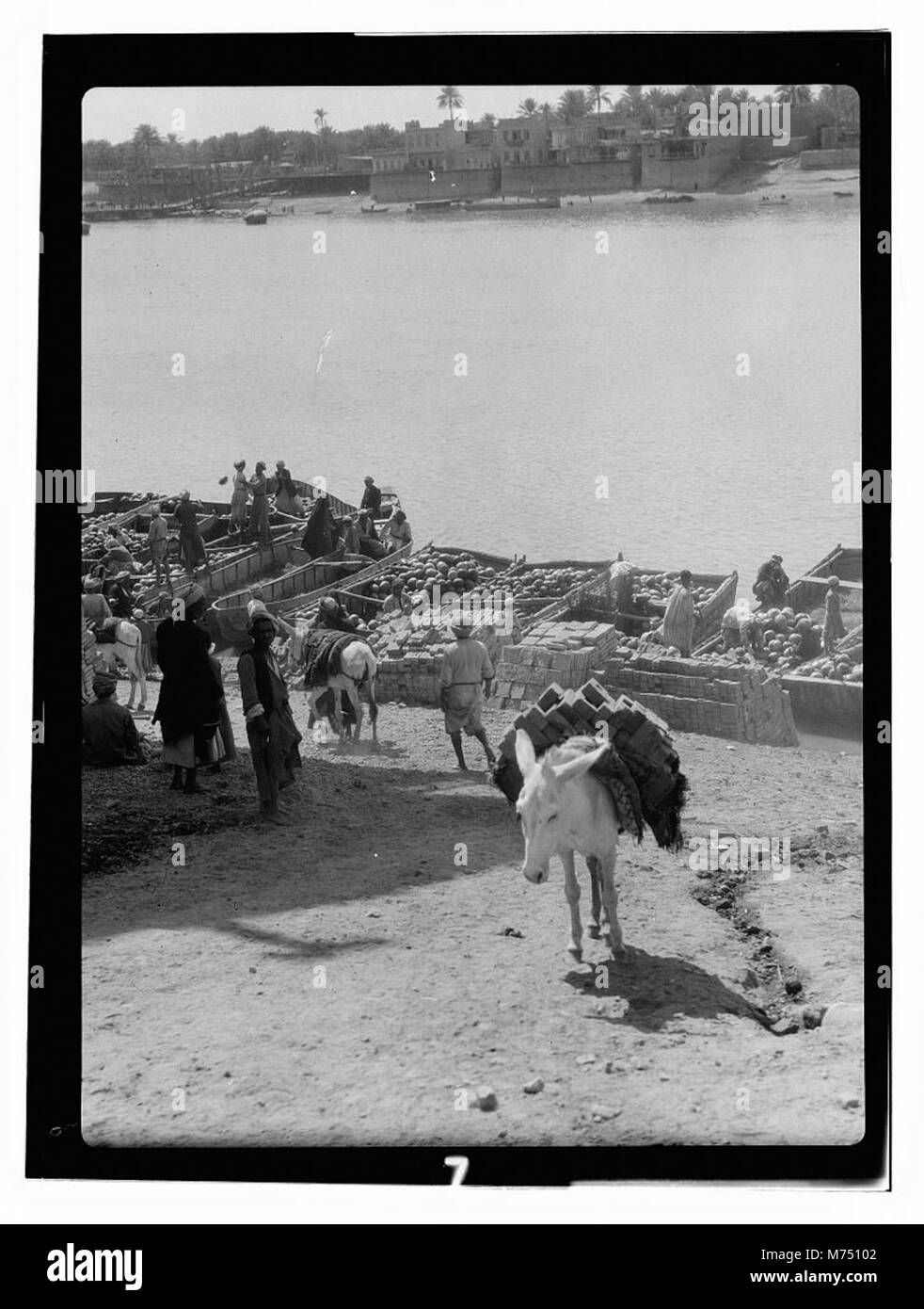 Cette image représente des bateaux en cours de déchargement sur une rivière en Irak, avec une ligne d'horizon de la ville en arrière-plan. Il met en lumière les activités de transport fluvial et de commerce qui sont essentielles à l’économie de la région. Banque D'Images