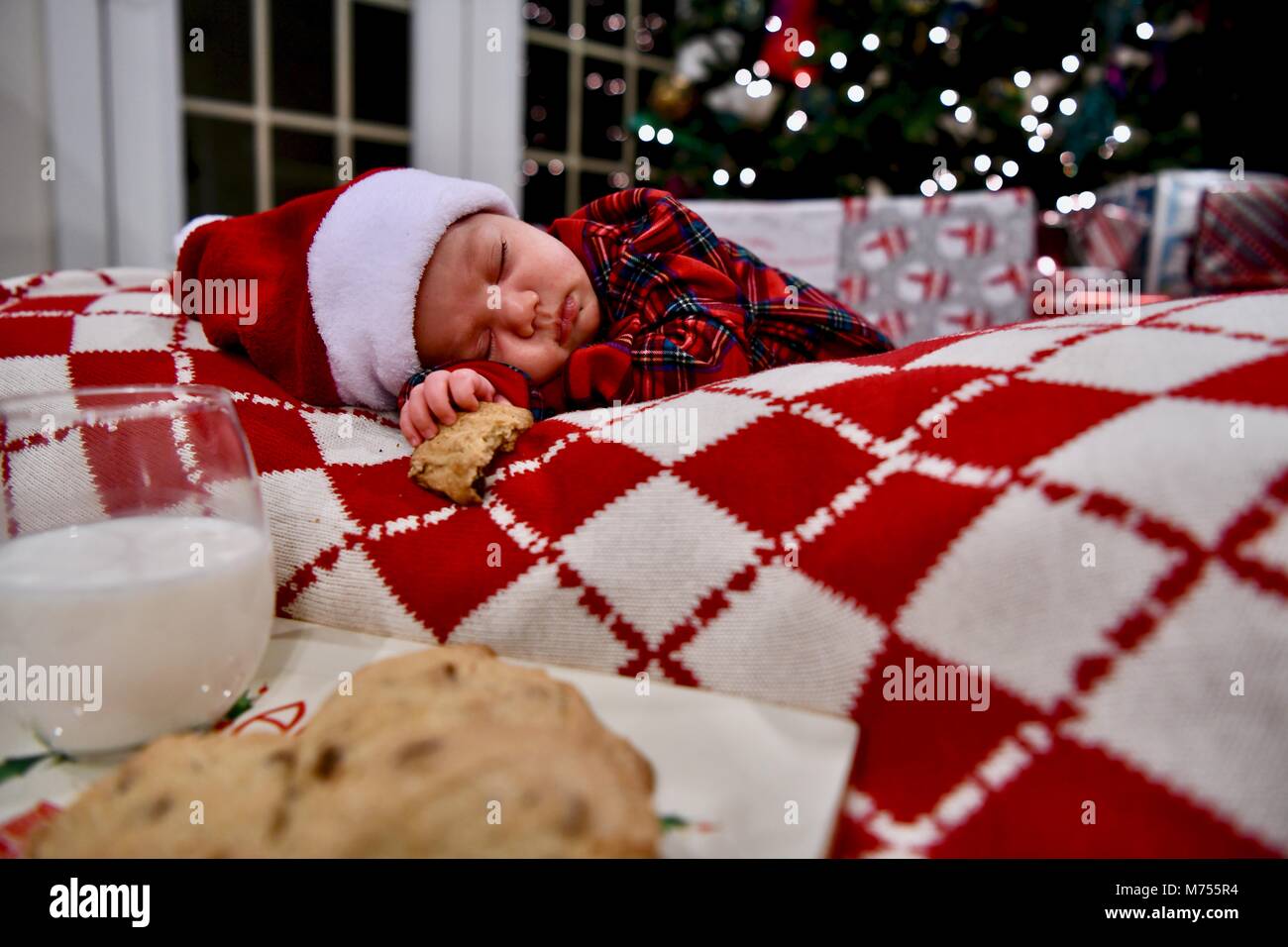 Bébé nouveau-né de dormir à côté de l'arbre de Noël à l'aide d'un témoin dans une main et verre de lait près de par Banque D'Images